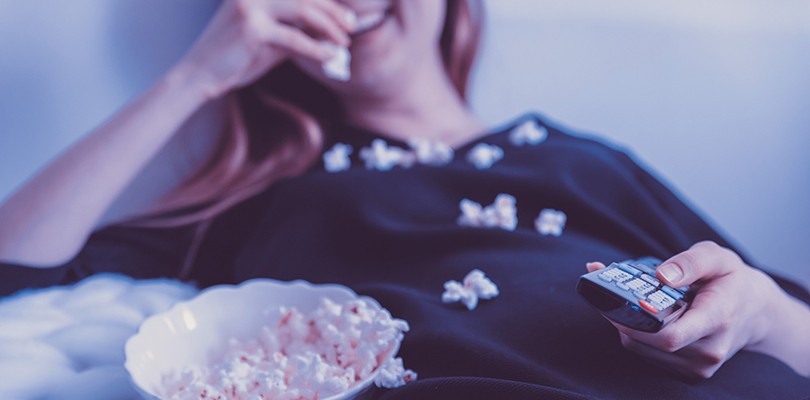 Woman laying on bed, eating popcorn