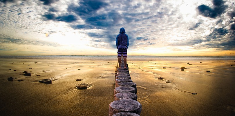 Man in Hooded Sweatshirt on a Beach at Sunrise