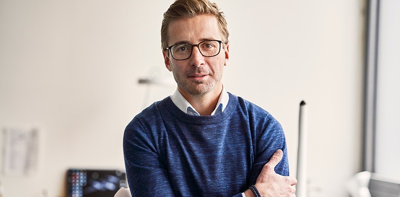 A self portrait of a male content marketer wearing glasses with his arm crossing his body, looking directly in to the camera.