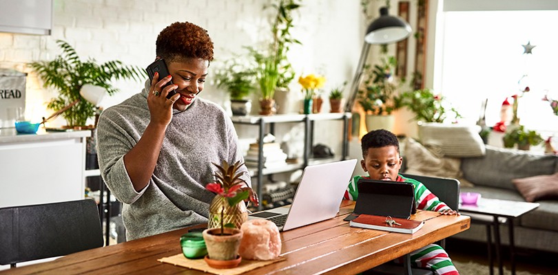 Mother talking on phone and in front laptop on the kitchen island and son on tablet