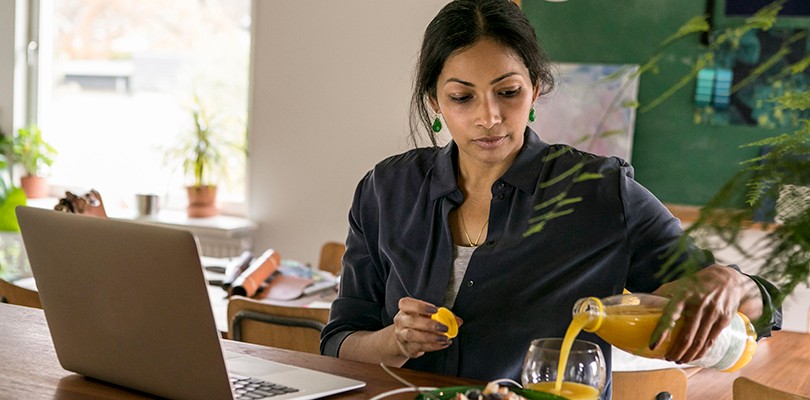 Female marketer pouring juice in glass with laptop on table in home office