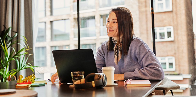 Woman in front of a large window smiling with a laptop