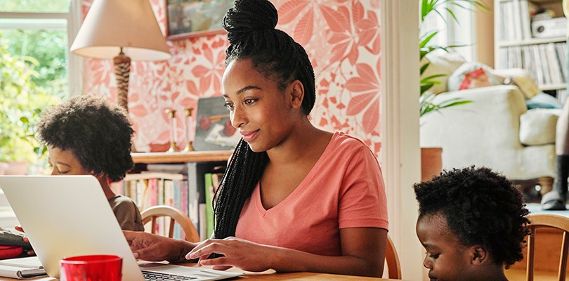 Woman sitting at table looking at laptop, two kids sitting next to her