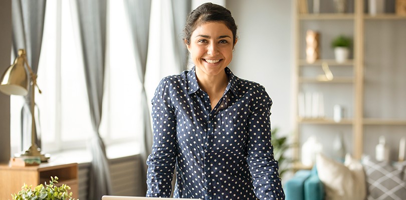 Happy female marketer looking at camera at home with laptop