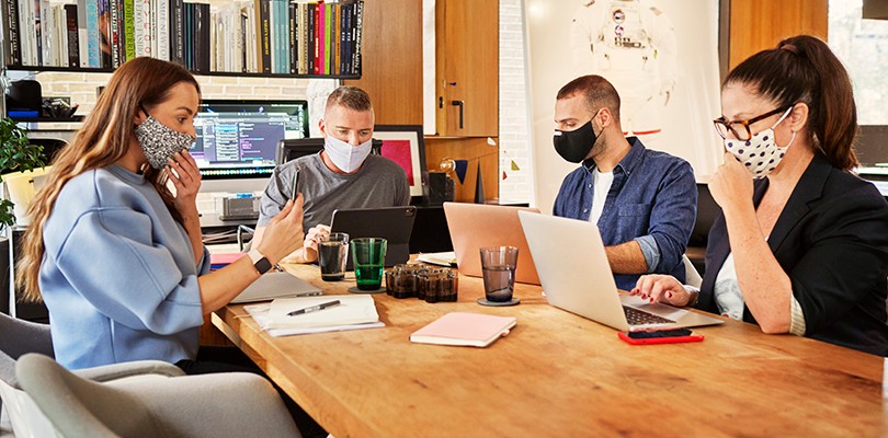 Group of men and women at work in a meeting room with masks on.