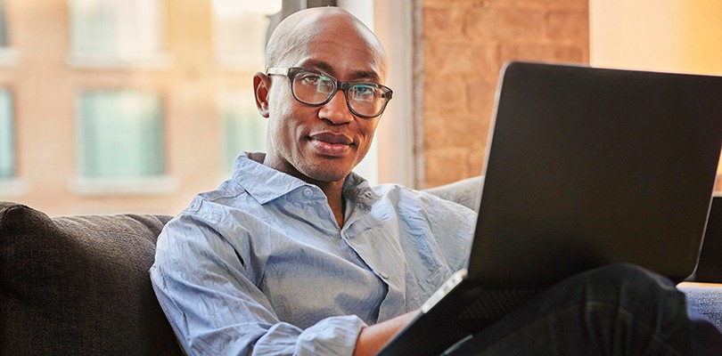 Man sitting on couch with a laptop, looking straight into the camera