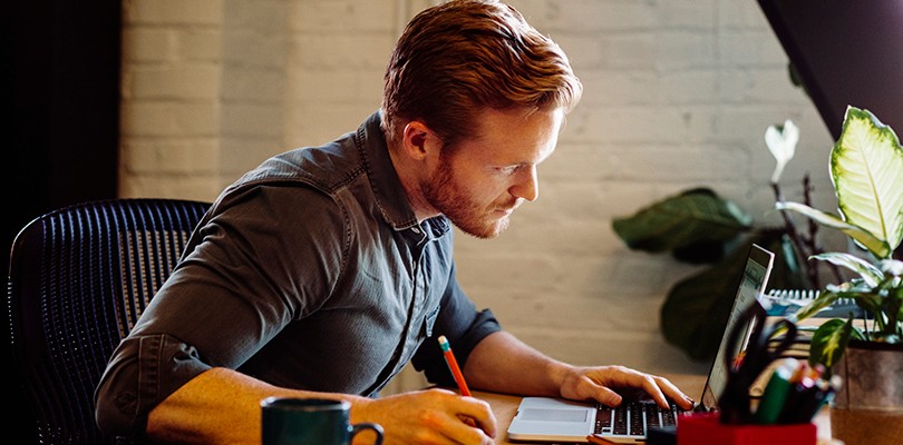 A man in deep focus at his laptop computer while sitting at a desk in an office.