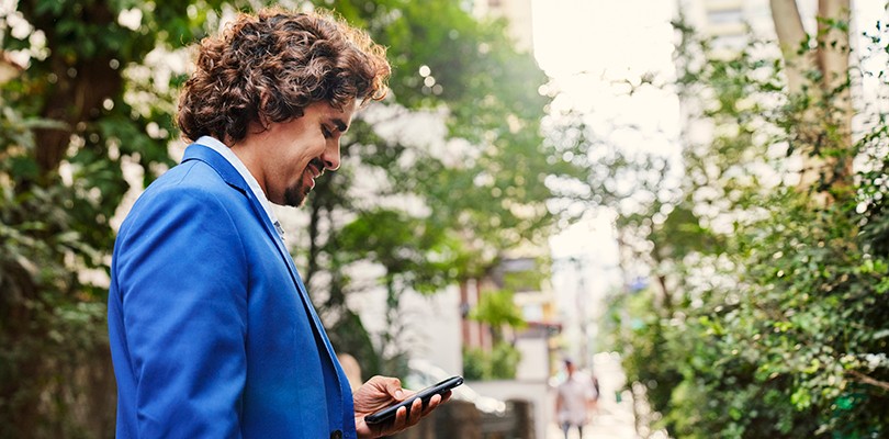 Side view of man standing outdoors smiling, while looking down at the phone in his hand.