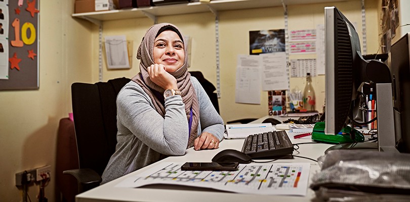 Female marketer smiling while sitting at her desk in an office with her hand under her chin.