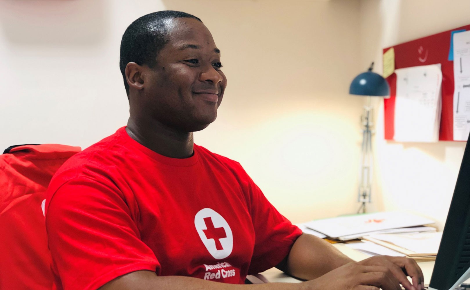 American Red Cross worker smiling and working at a desk on a computer