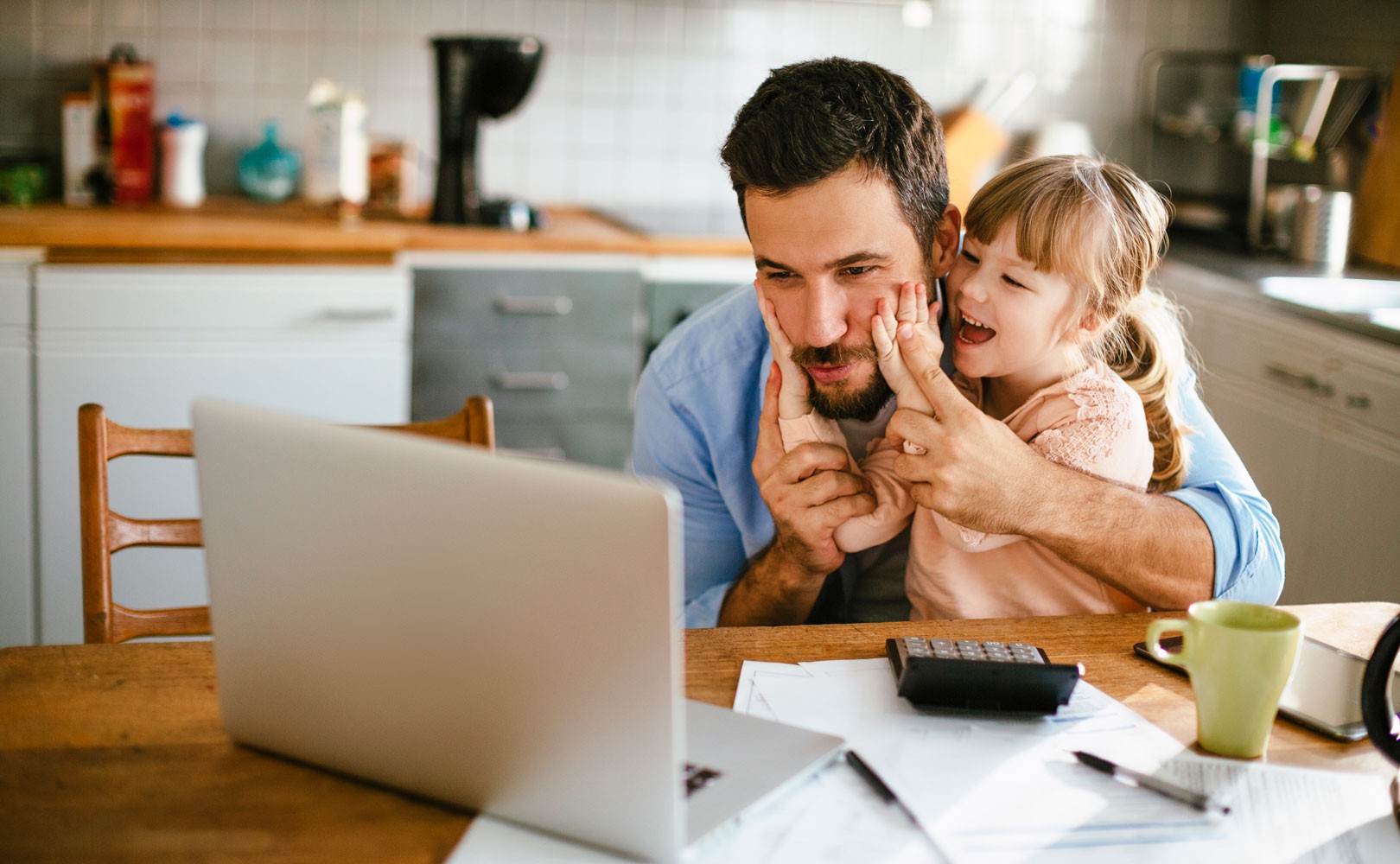 Photo of father and daughter sitting at kitchen table with a laptop on it