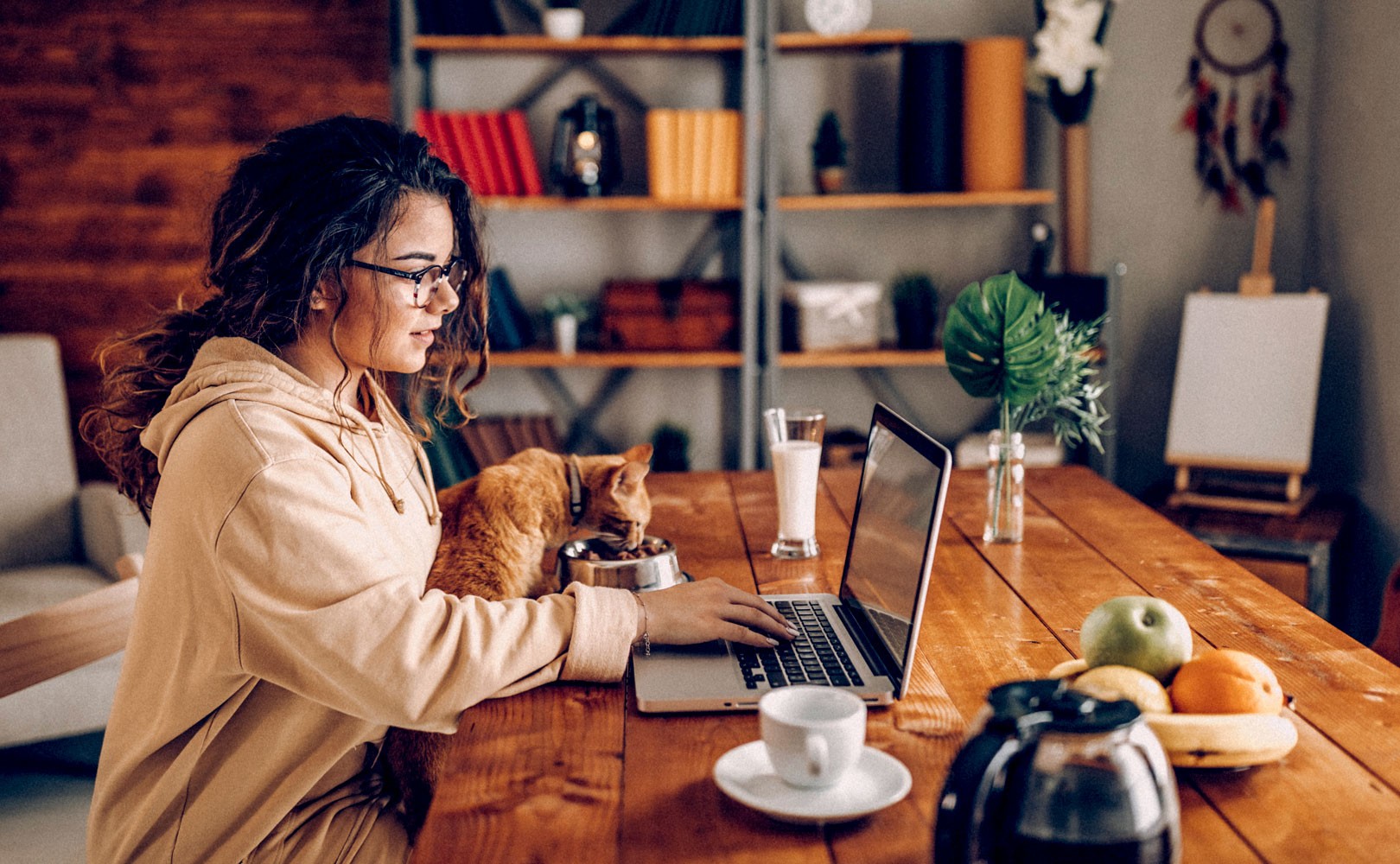 Photo of woman working from home at a table with her cat eating next to her