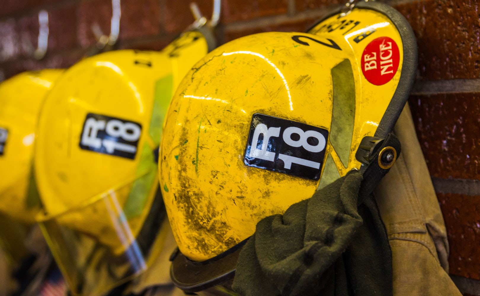 Photograph of firefighters hats and jackets hanging from hooks on wall