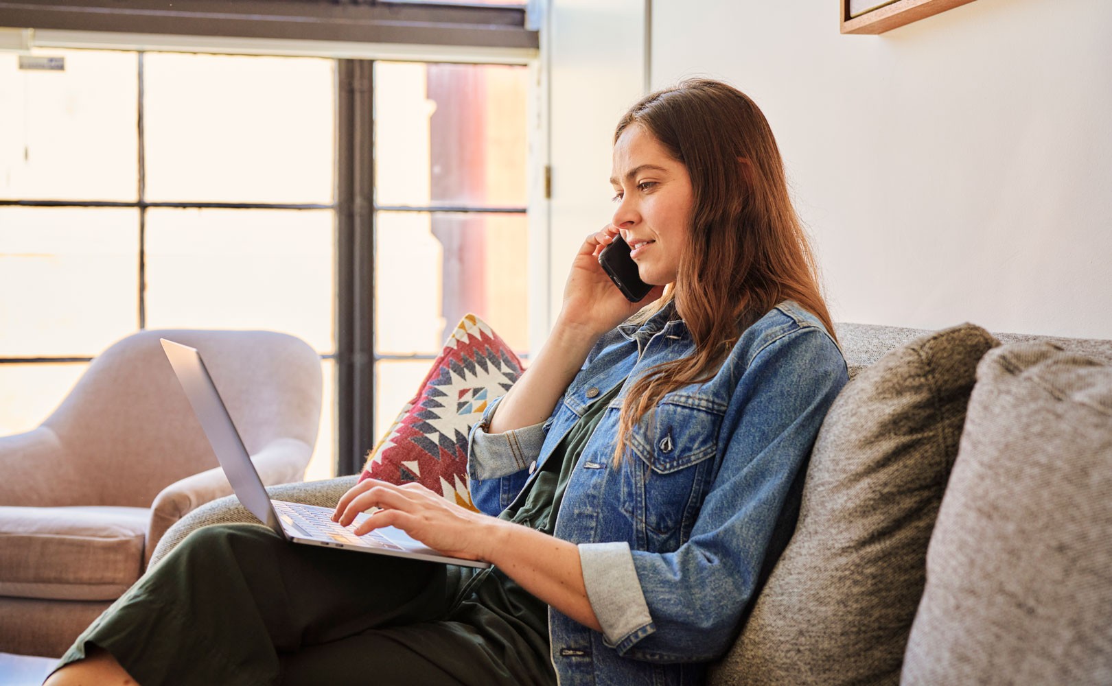Photo of woman sitting on couch with laptop and talking on phone