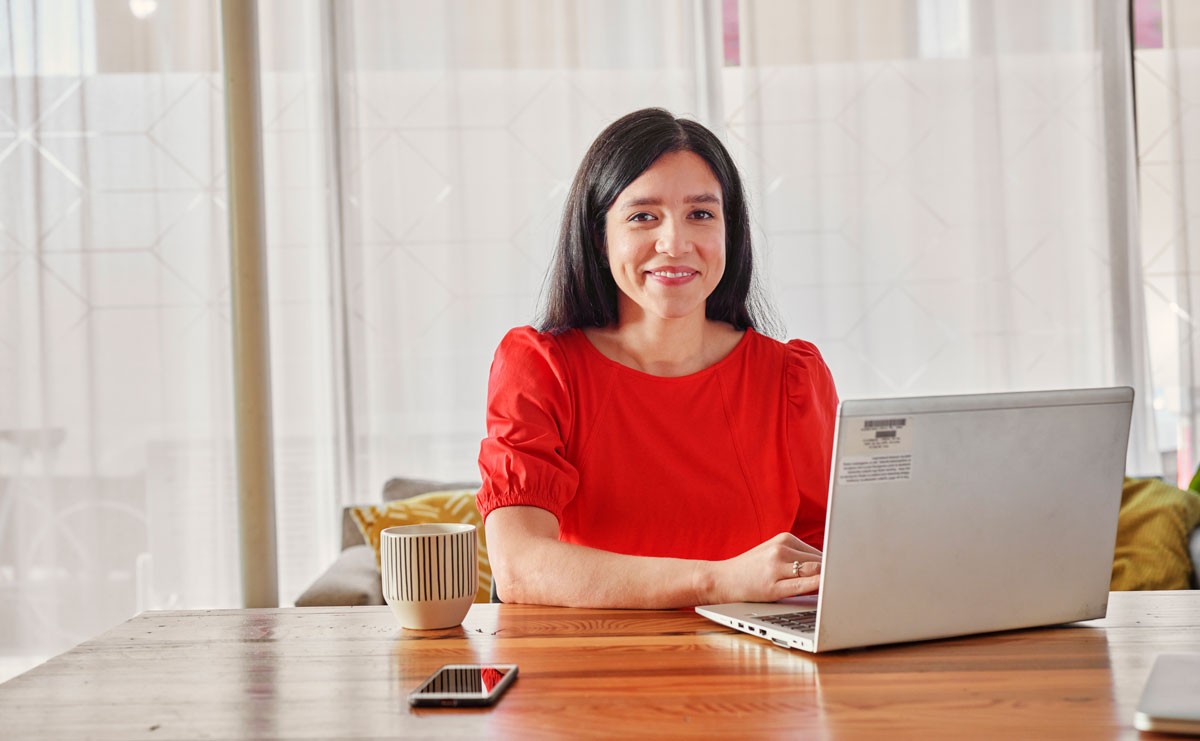 woman sitting at table with her computer smiling at the camera