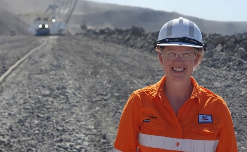 Photo of BHP employee, a smiling woman wearing a protective hat, working outdoors