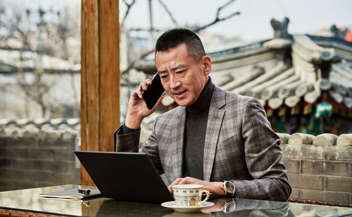 Photo of man working on laptop outside while talking on phone