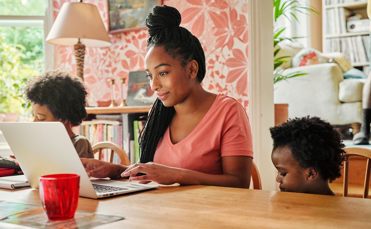 Photo of mom reading on laptop with two kids nearby