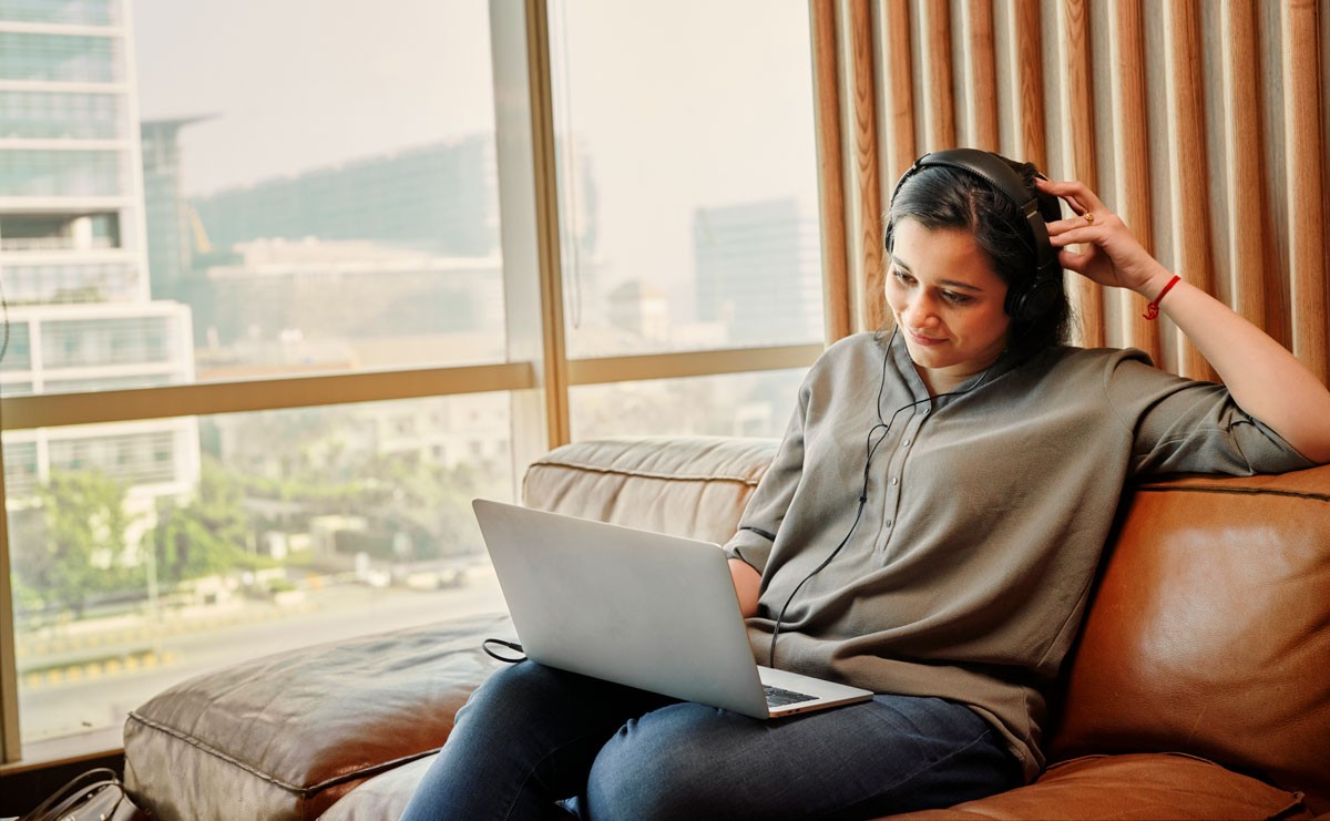 Photograph of woman with headphones watching a virtual event on her laptop
