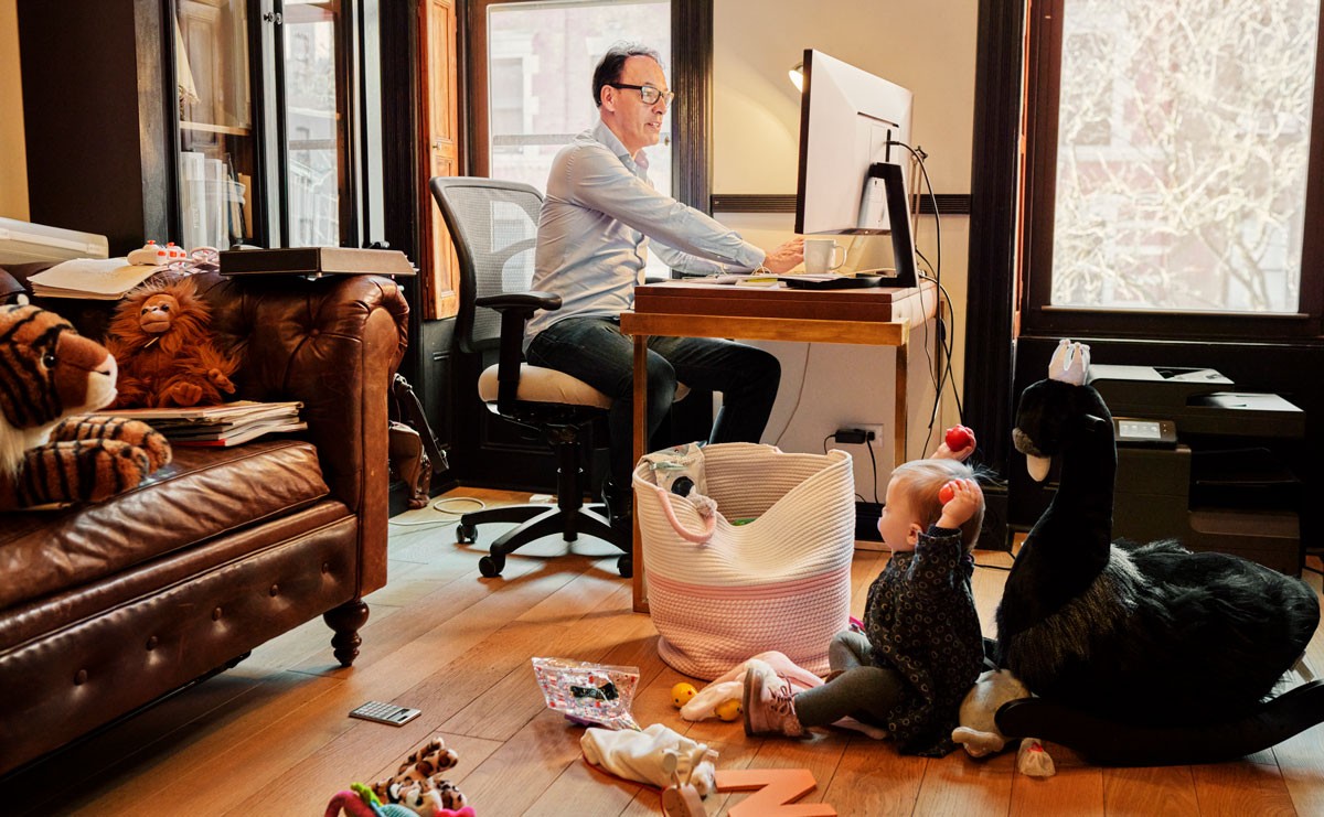 Photo of man working from home with toddler playing next to his desk