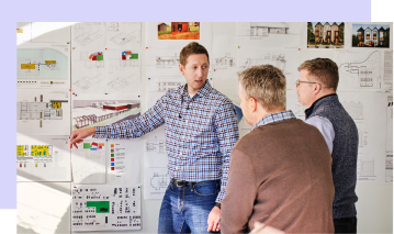 Three individuals having a brainstorming session next to a white board.