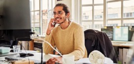 Una persona che parla al telefono mentre lavora su un laptop.