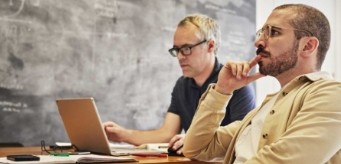 Deux personnes assises à côté d’un tableau.