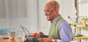 An individual smiling and using their laptop at home.