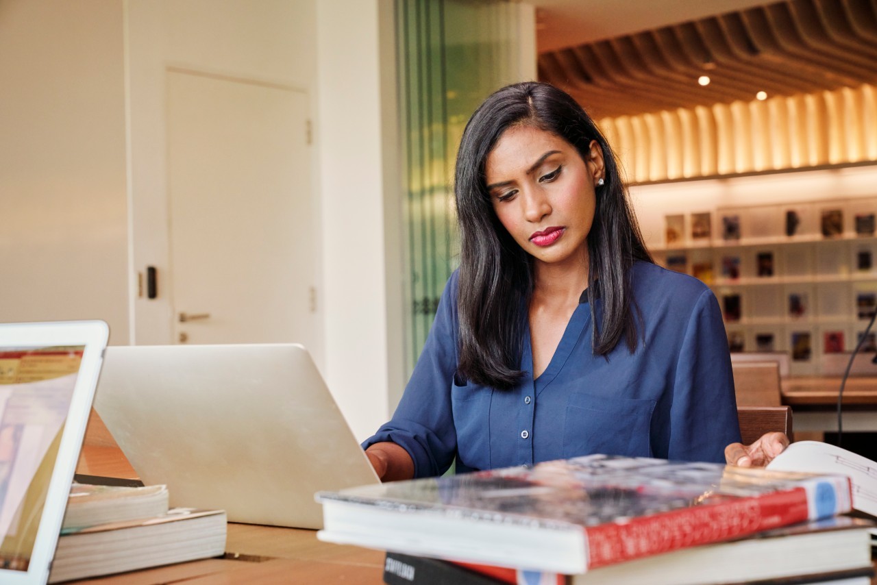 woman sitting at desk looking at a laptop and book