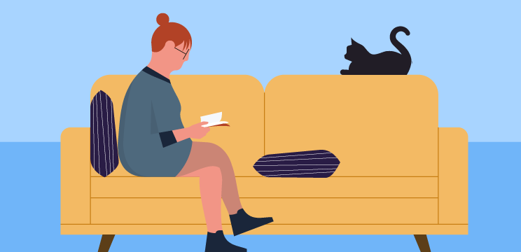 A person reading a book on a sofa next to a sleeping cat.