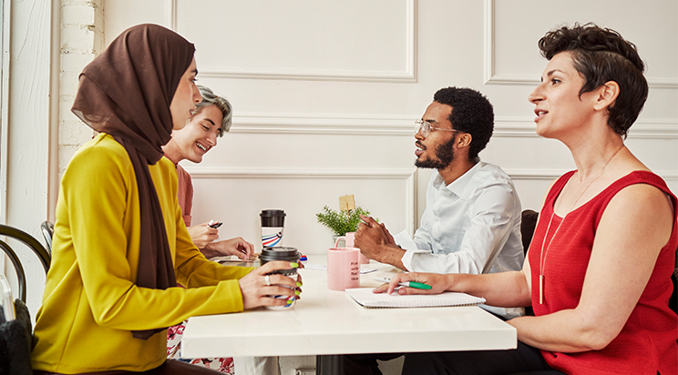 A diverse group of employees learns together over coffee at work.