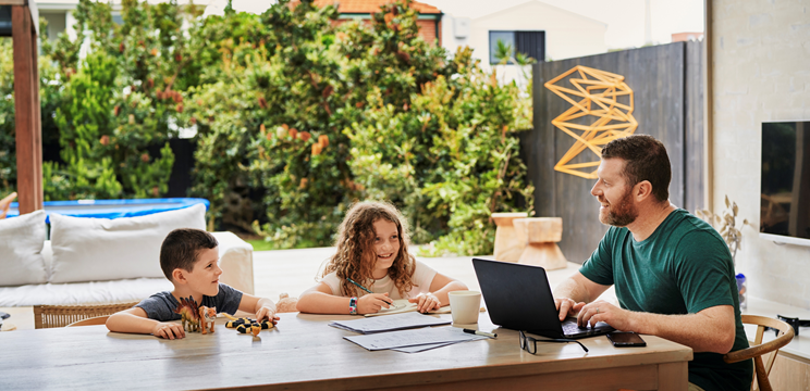 Image of a man working from home with his two children sitting beside him at the table.