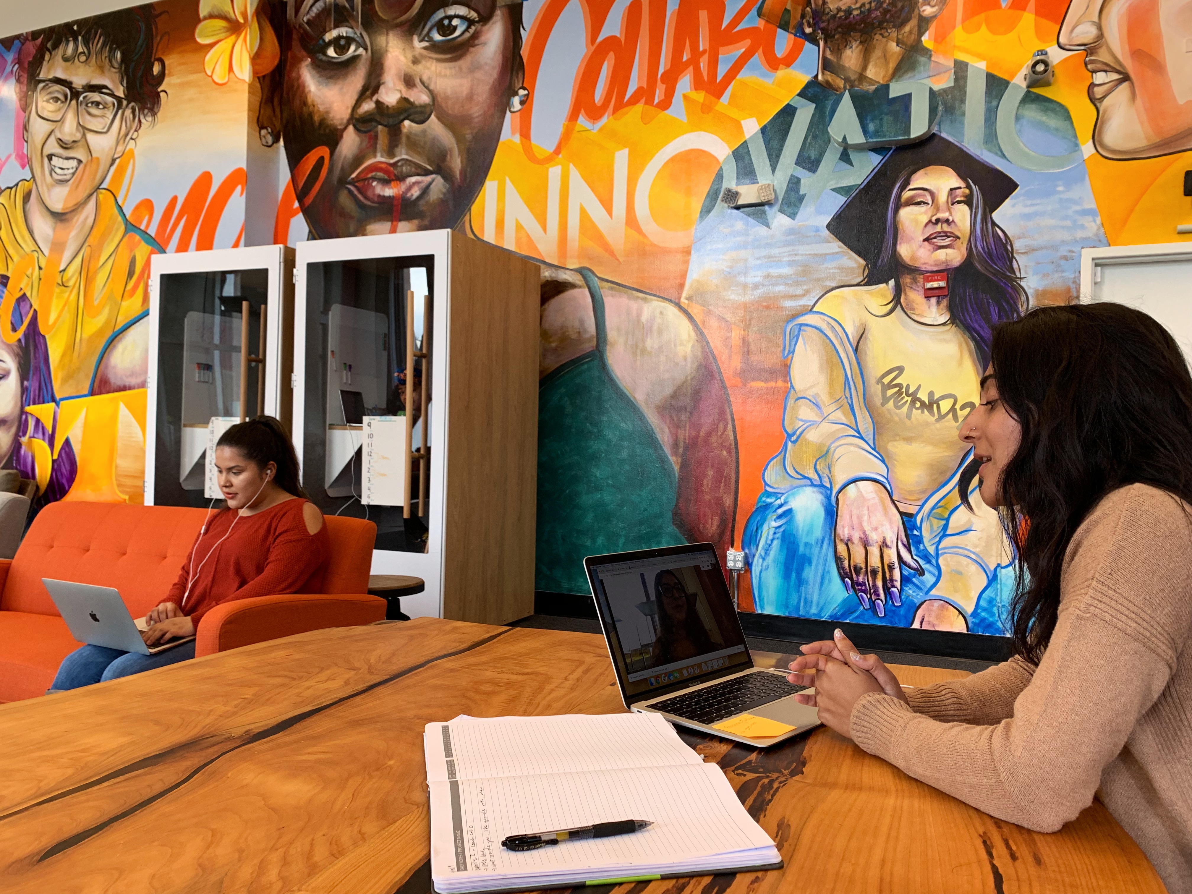 A Beyond 12 coach has a virtual coaching session beside a mural of diverse college students.