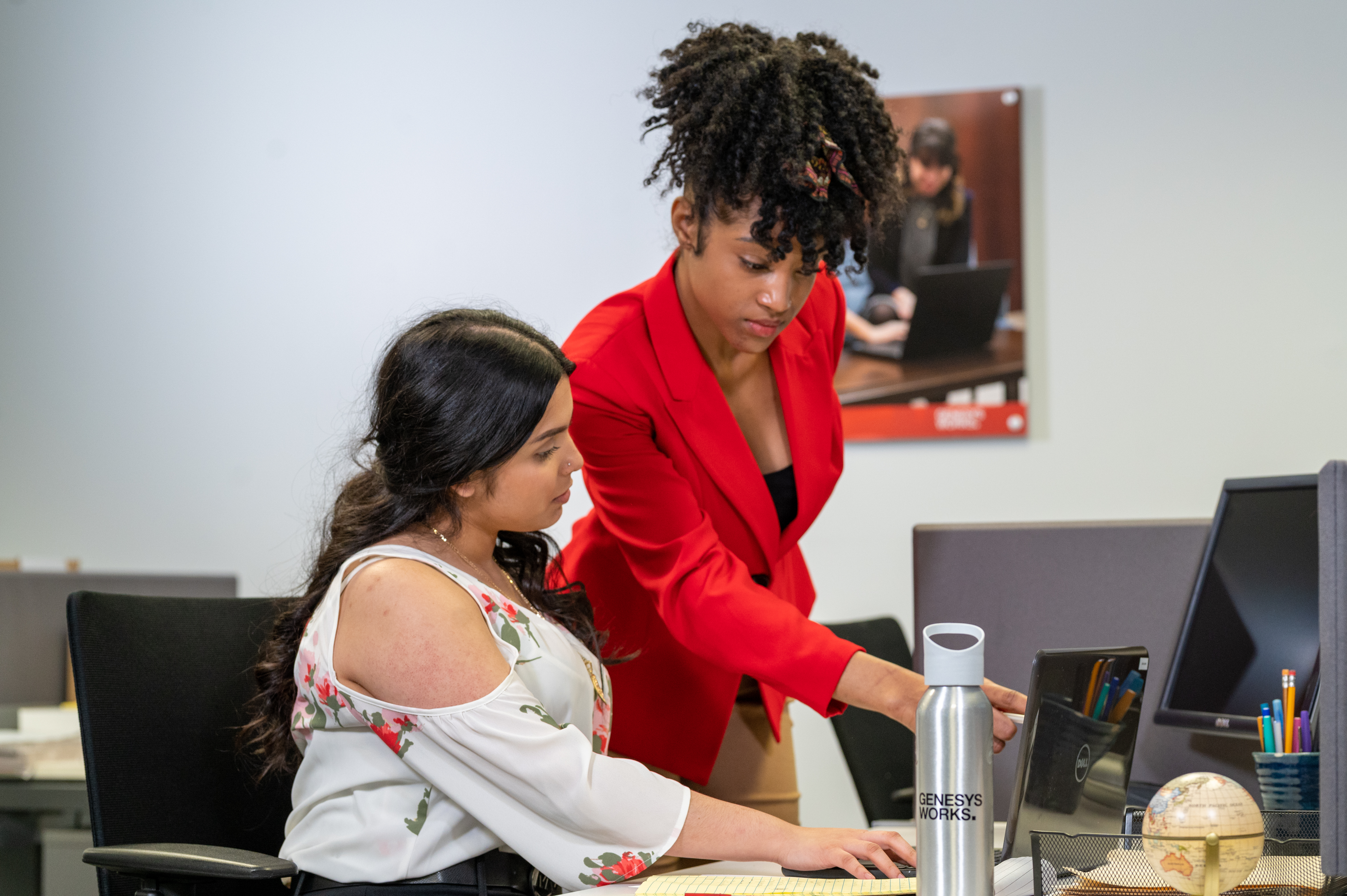 A Genesys Works team member collaborates with a young professional at a laptop.