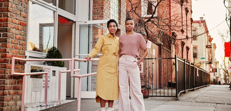 Two team members stand side by side outside a building, smiling at the camera.